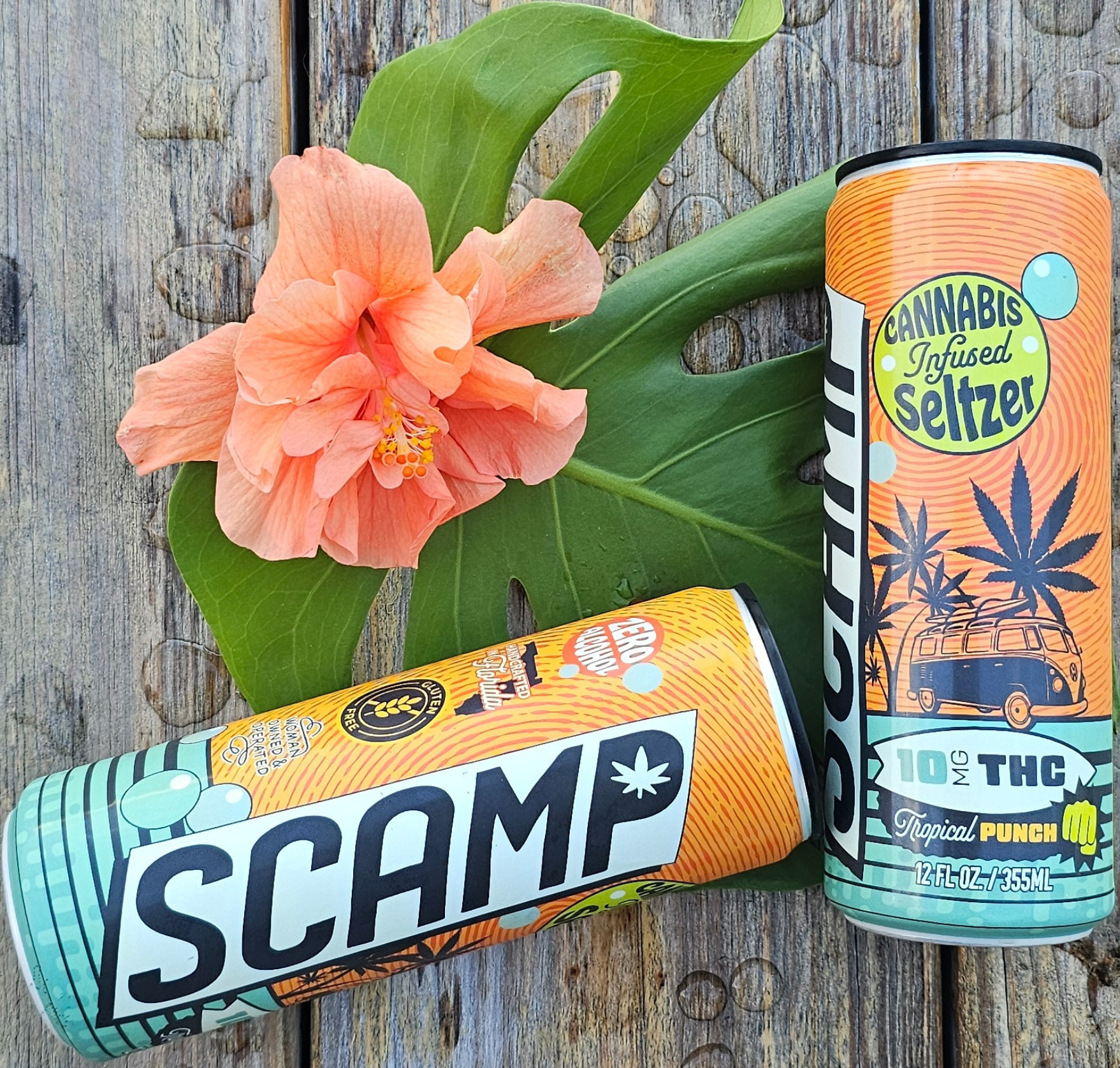 Two cans of SCAMP Cannabis Infused Seltzer on a wooden surface with a flower and leaf.